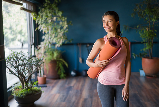 Portrait of a Latin American woman at the gym holding a yoga mat and smiling - fitness concepts