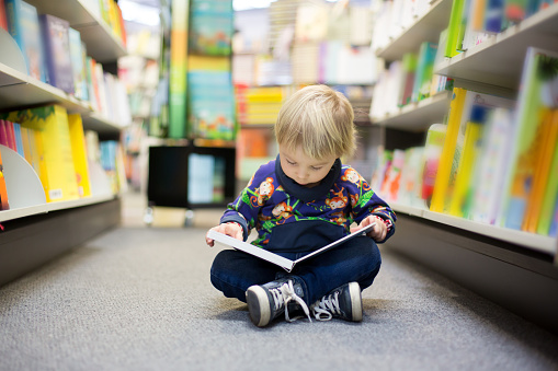 Adorable little boy, sitting in a book store and read book