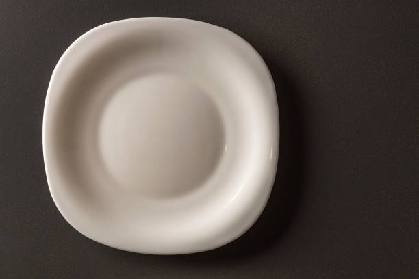 istock Close up view of white  square shaped plate on black background. Black and white background. Eating concept background. 1306383499