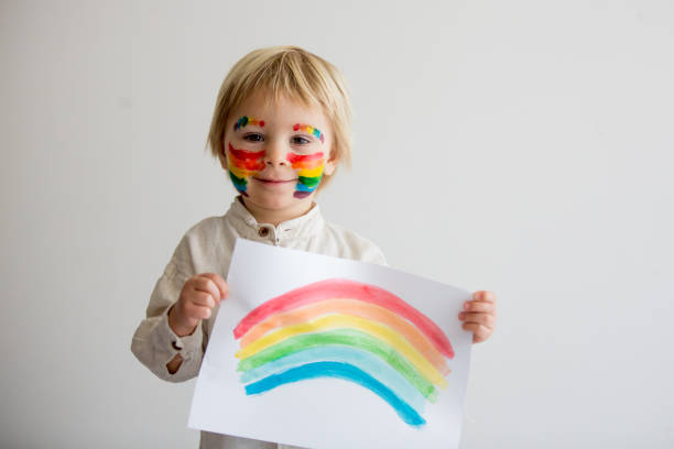 istock Beautiful blond toddler boy with rainbow painted on his face and messy hands 1306383563