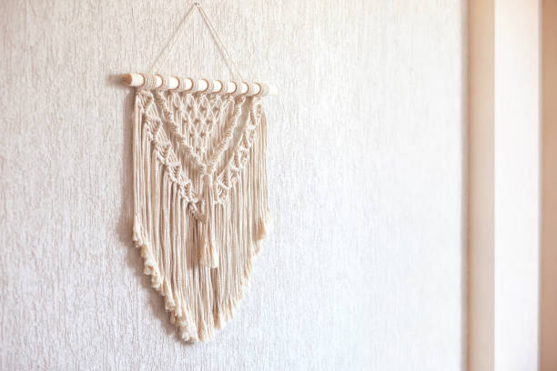 istock Handmade macrame. 100% cotton wall decoration with wooden stick hanging on a white wall. Copy space.  Female hobby.  ECO friendly modern knitting DIY natural decoration concept in  interior 1306383968