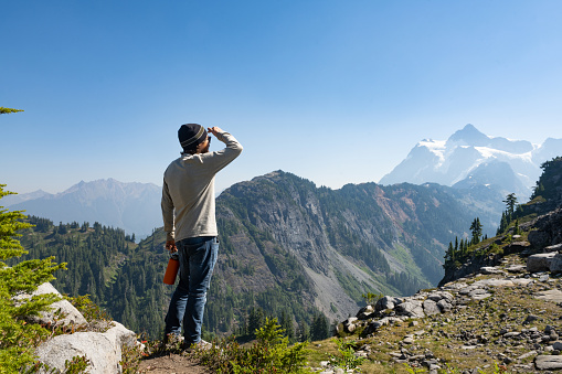 Tired hiker with backpack and trekking poles rests by a huge boulder in the mountains