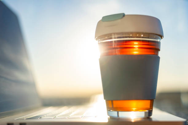 tasse réutilisable en verre au soleil. la tasse est assise à côté d’un ordinateur portable. - coffee to go flash photos et images de collection