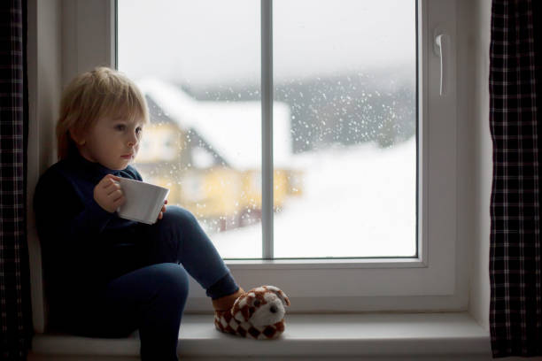 istock Toddler child, sitting on the window, watching the snow falling 1306388278