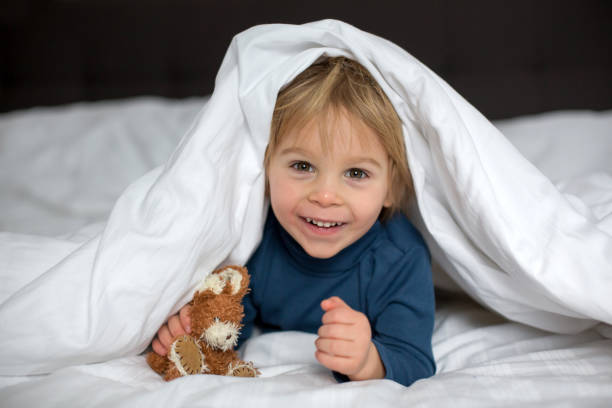 istock Cute child, lying in bed, playing with little stuff toy 1306388406