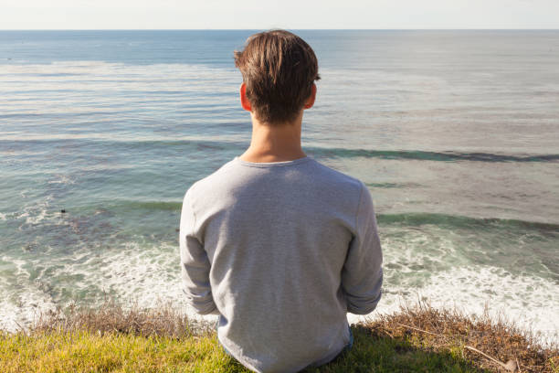istock Relaxed young man sitting alone on top a cliff looking at the ocean view. 1306392849