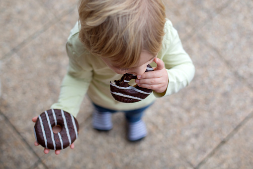 Sweet toddler child, playing with chocolate donuts, eating them happily
