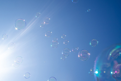 Soap bubbles flying in the air against a clear blue sky with sunbeams.