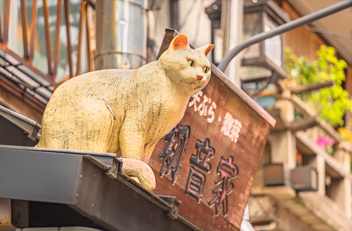 tokyo, japan - february 28 2021: Sculpture depicting a white cat looking down on a roof in the Yanaka-Ginza shopping street known as a holy place for cats in the old-fashioned district of Yanesen.