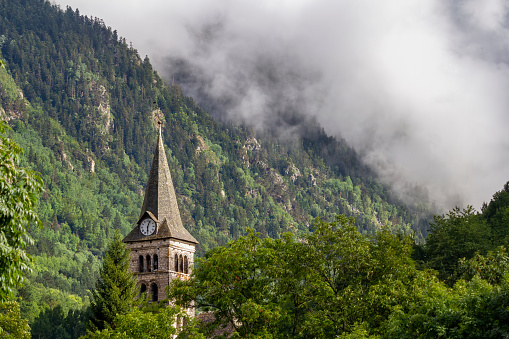 bell tower with a clock in a mountain village. Clouds cover a hillside in the background, in Arties, Valle de Aran Lleida, Spain