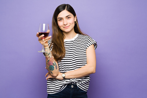 Portrait of an attractive young woman making eye contact while holding a glass of wine. Smiling woman drinking and enjoying red wine