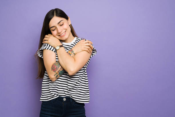 Loving hispanic woman embracing herself and feeling happy Cute happy young woman smiling and hugging herself in front of a purple background with copy space. Beautiful woman doing self-care and self-love activities hugging self stock pictures, royalty-free photos & images