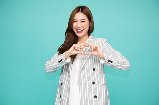 Asian business woman in suit showing heart sign isolated on green background, Speading love and happiness concept