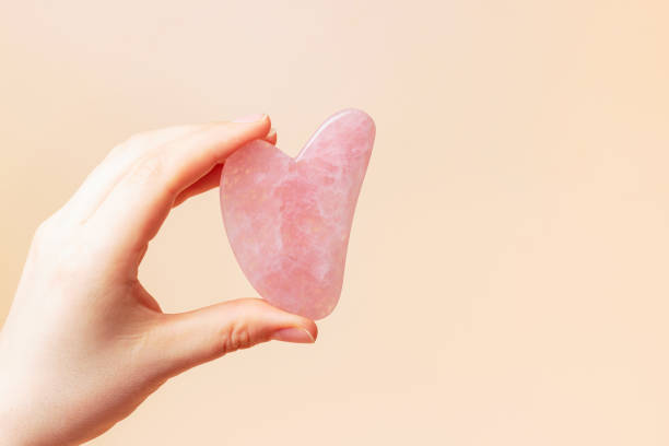 A female hand holding gua sha face massager on brown background.