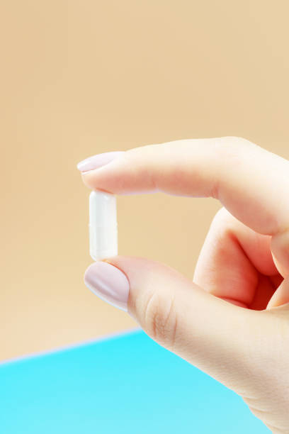 istock Female hand holding capsule close-up on brown background. 1306405550