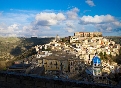 Ragusa Ibla, Sicily: Hillside cityscape panorama, with a vibrant cloudy blue sky background. Ragusa Ibla is a UNESCO World Heritage Site.