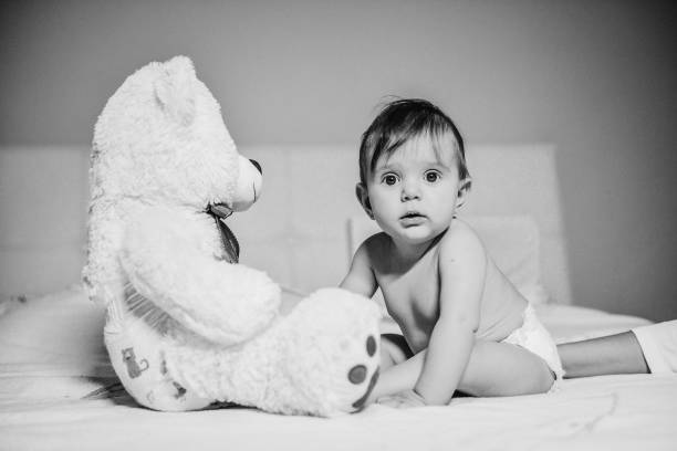 istock Baby girl sitting on bed playing with teddy bear 1306408809
