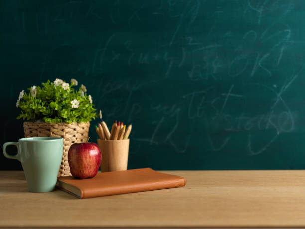 istock Study table with notebook, apple, pencils and plant pot in classroom with blackboard background 1306412001