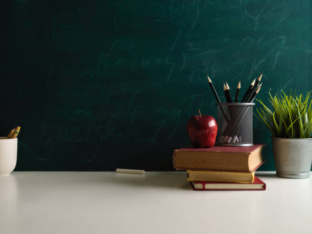 istock Close up view of books and school elements on study table in class room with chalkboard wall 1306412021