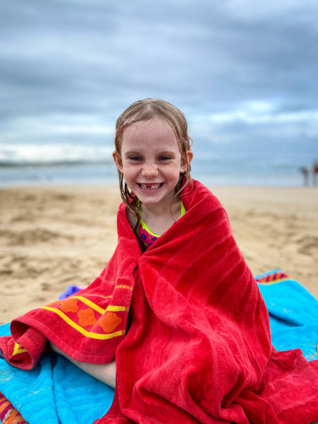 istock Happy young girl sitting on the beach wrapped in a red towel 1306415607