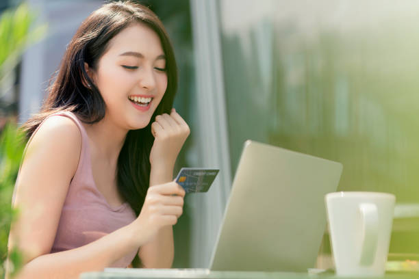 attraktive erwachsene asiatische weibliche glück online mit laptop hand halten kreditkarte und smartphone für kaufprodukt mit hintergrund des baugartens outdoor business-ideen-konzept - easy money stock-fotos und bilder