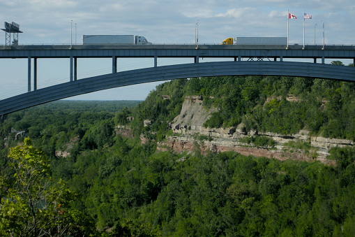 Two trucks, on the Lewiston-Queenston bridge, delivering goods over the lush Niagara gorge during the summer.