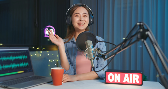 asian woman with microphone is recording podcast at home or studio in the evening