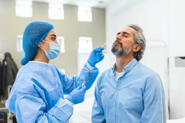 Healthcare worker with protective equipment performs coronavirus swab on elderly man. Nose swab for Covid-19. Healthcare worker with protective equipment performs coronavirus swab on elderly man. Nose swab for Covid-19. pcr device photos stock pictures, royalty-free photos & images