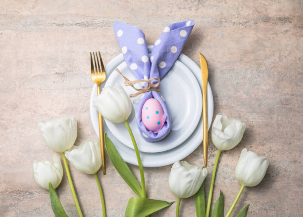 istock Easter holiday table setting with bunny  from egg on white plate and tulips flowers.  Gray concrete table, top view with copy space for text. Happy Easter background 1306430570
