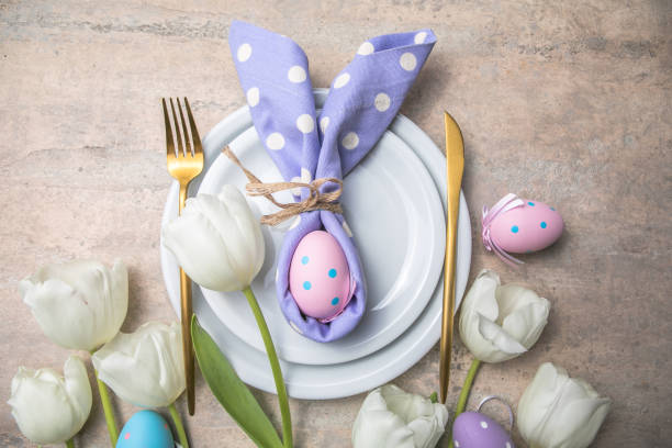 istock Easter holiday table setting with bunny  from egg on white plate and tulips flowers.  Gray concrete table, top view with copy space for text. Happy Easter background 1306430573