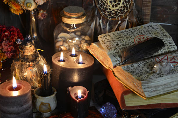 istock Open grimoire book of spells, burning candles, runes and ritual objects on witch table. 1306434998
