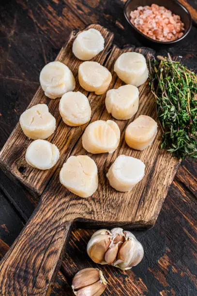 Photo of Steamed scallops meat on a wooden board. Dark wooden background. Top view