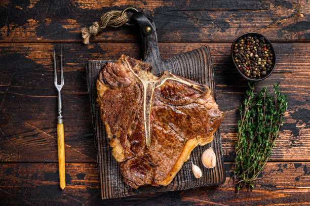 rôti t-bone ou viande de bœuf porterhouse steak sur une planche à découper en bois. fond en bois foncé. vue supérieure - porterhouse steak photos et images de collection