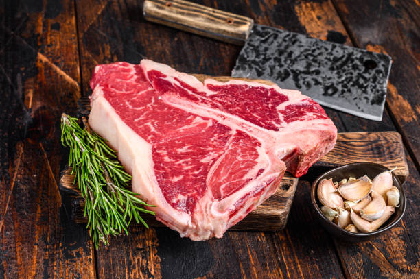 raw t-bone beef meat steak with herbs on a wooden cutting board. dark wooden background. top view - beef meat t bone steak steak imagens e fotografias de stock