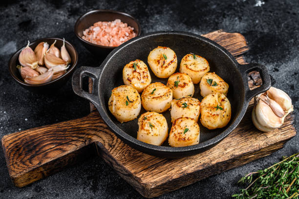 istock Fried scallops with butter sauce in a pan. Black background. Top view 1306437728