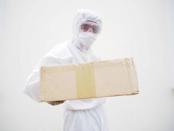 istock Young man in PPE suite uniform while holding cardboard boxes in medical rubber gloves and mask. coronavirus or COVID-19 concept isolated white background 1306445152