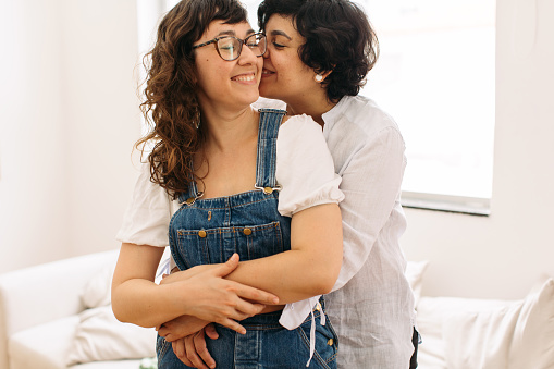 Portrait of affectionate couple holding each other. Woman holding her girlfriend from behind and kissing her on cheeks.