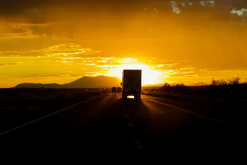 A tractor-trailer traveling west is silhouetted by the bright, setting sun Interstate-40 in Arizona in the Southwest USA.