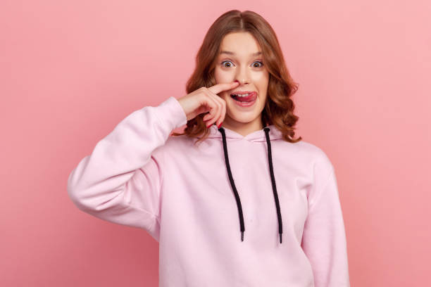 portrait of funny teen curly haired girl in hoodie drilling nose fooling around, showing tongue out and picking nose with comical silly expression - rudeness ugliness clothing people imagens e fotografias de stock