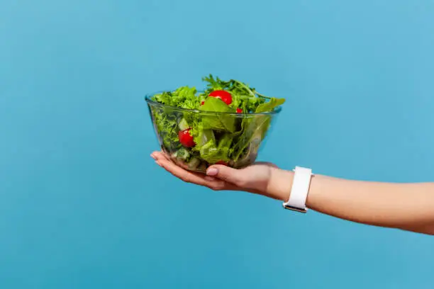 Photo of Close up female hand holding big glass bowl with green salad from fresh red tomatoes and lettuce leaves, organic nutrition, healthy eating, detox diet