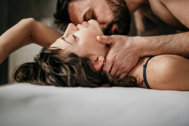 Kissing your neck and feeling your skin Side view photo of a beautiful couple in bed, being gentle and sensual. Handsome guy with a beard on top of the beautiful brunette is kissing her neck while her eyes are closed. Making love concept sensuality stock pictures, royalty-free photos & images