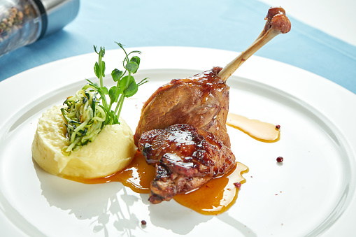 Pierna de pato confitada con salsa dulce adornada con puré de papas en un plato blanco en un mantel azul photo