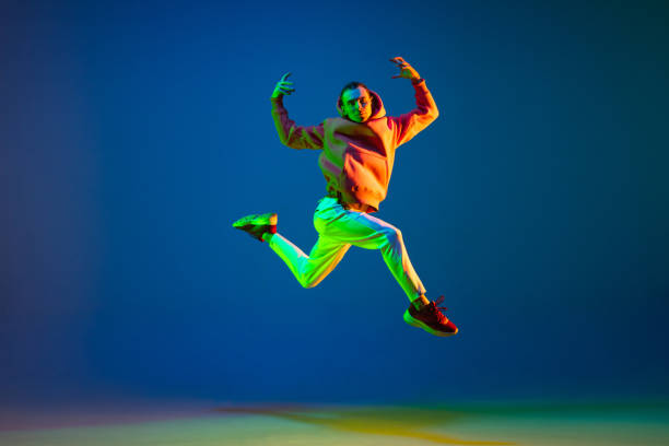 istock Young male dancer jumping isolated over on blue background in neon light 1306462716