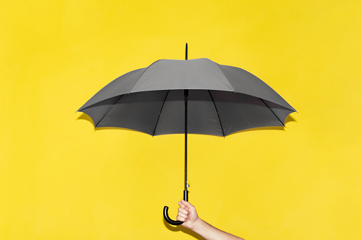 A man holds in his hand a gray umbrella against the background of a yellow wall