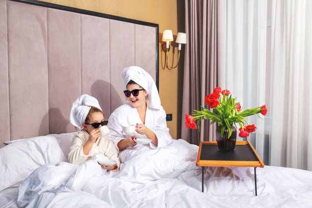 feliz hermosa familia madre e hija en el dormitorio en la cama en toallas y gafas de sol organizaron una fiesta de moda - bathrobe women cup towel fotografías e imágenes de stock