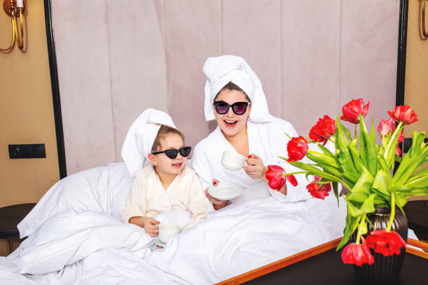 szczęśliwa piękna matka rodzinna i córka w sypialni na łóżku w ręcznikach i okularach przeciwsłonecznych urządzili modną imprezę - flower spring bouquet child zdjęcia i obrazy z banku zdjęć