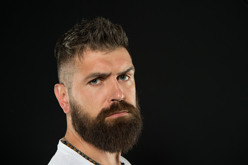Bring more style to bearded face. Bearded man on black background. Serious bearded hipster with stylish haircut. Brutal caucasian guy wearing mustache and beard on bearded face, copy space