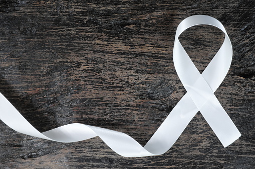Top view of white ribbon on dark wood background. Lung cancer awareness concept.