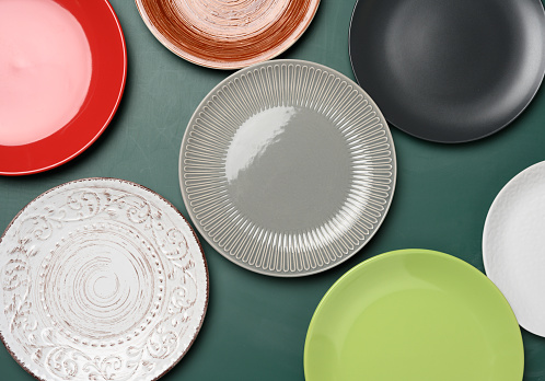 empty round multicolored ceramic plates on green background, top view