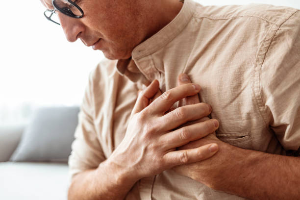 I'm having a little trouble breathing Severe heartache, man suffering from chest pain, having heart attack or painful cramps, pressing on chest with painful expression. Photo of Mature man suffering from chest pain at home during the day. endocarditis stock pictures, royalty-free photos & images